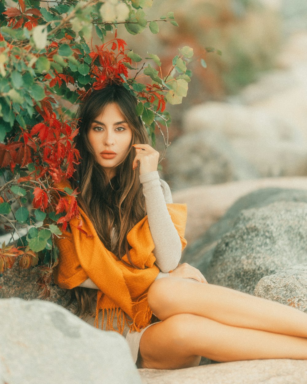 a beautiful woman sitting on a rock next to a tree