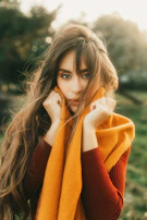 Woman smiling warmly while wrapping a bright, original snood scarf around her neck outdoors.