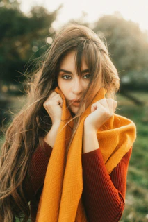 Woman smiling warmly while wrapping a bright, original snood scarf around her neck outdoors.