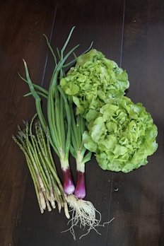 Fresh green vegetables including chard, celery, spring onions, and fennel arranged on a rustic wooden table.