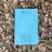 A book with a bright blue cover featuring the title 'TRADUTOR DE CHUVAS' and the author's name, Mia Couto, is placed on a bed of dry, brown leaves. The cover includes abstract yellow and white linear designs.
