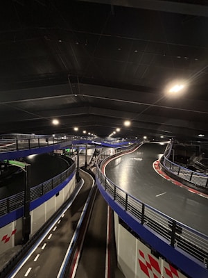 An indoor go-kart track with elevated sections and multiple curves, featuring blue barriers and overhead lights. The environment is industrial, with a dimly lit atmosphere.