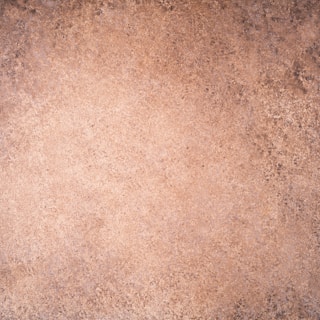 A textured surface with an earthy hue, exhibiting a rough, speckled pattern similar to stone or marble. The colors transition subtly across the surface, creating a natural look.