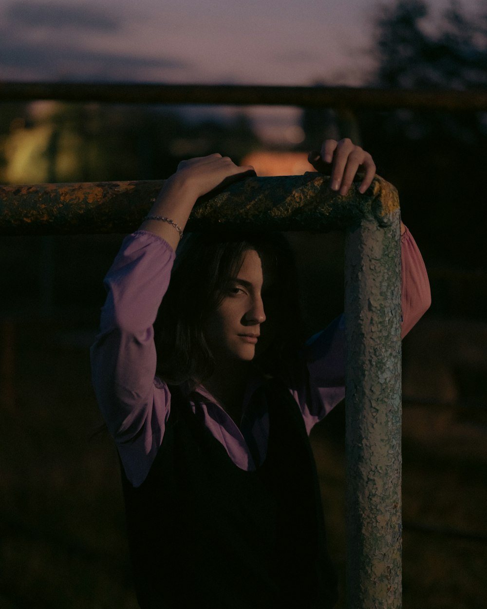 a woman in a pink shirt and black vest holding onto a metal pole