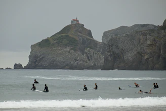 Surfers paddling out towards the 'Derechón' wave with volcanic cliffs in the background.