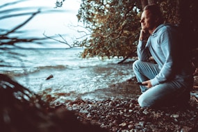 a man sitting on a beach next to a body of water