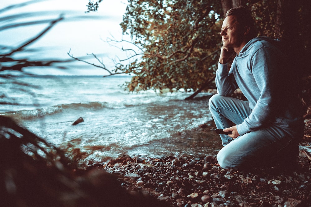 a man sitting on a beach next to a body of water