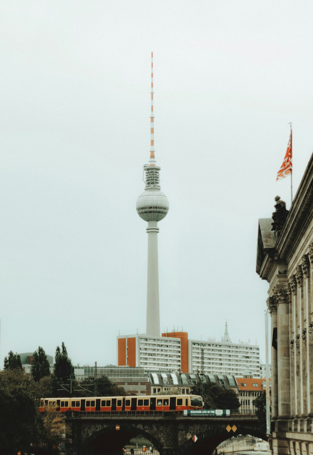 a train traveling past a tall building with a tv tower in the background