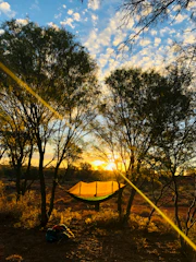 A side view of a Golite hammock set up on a rocky bluff, overlooking a mountain valley at sunset.