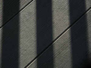 Dark shadows cast diagonal lines over a textured surface, creating a pattern of light and shade across the frame.