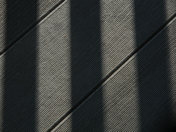 Dark shadows cast diagonal lines over a textured surface, creating a pattern of light and shade across the frame.