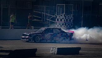 The car crossing the finish line with a trail of smoke behind on a sunny day.