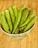 A ceramic bowl filled with fresh green okra pods is placed on a wooden surface. The okra pods appear fresh with a slightly glossy texture.