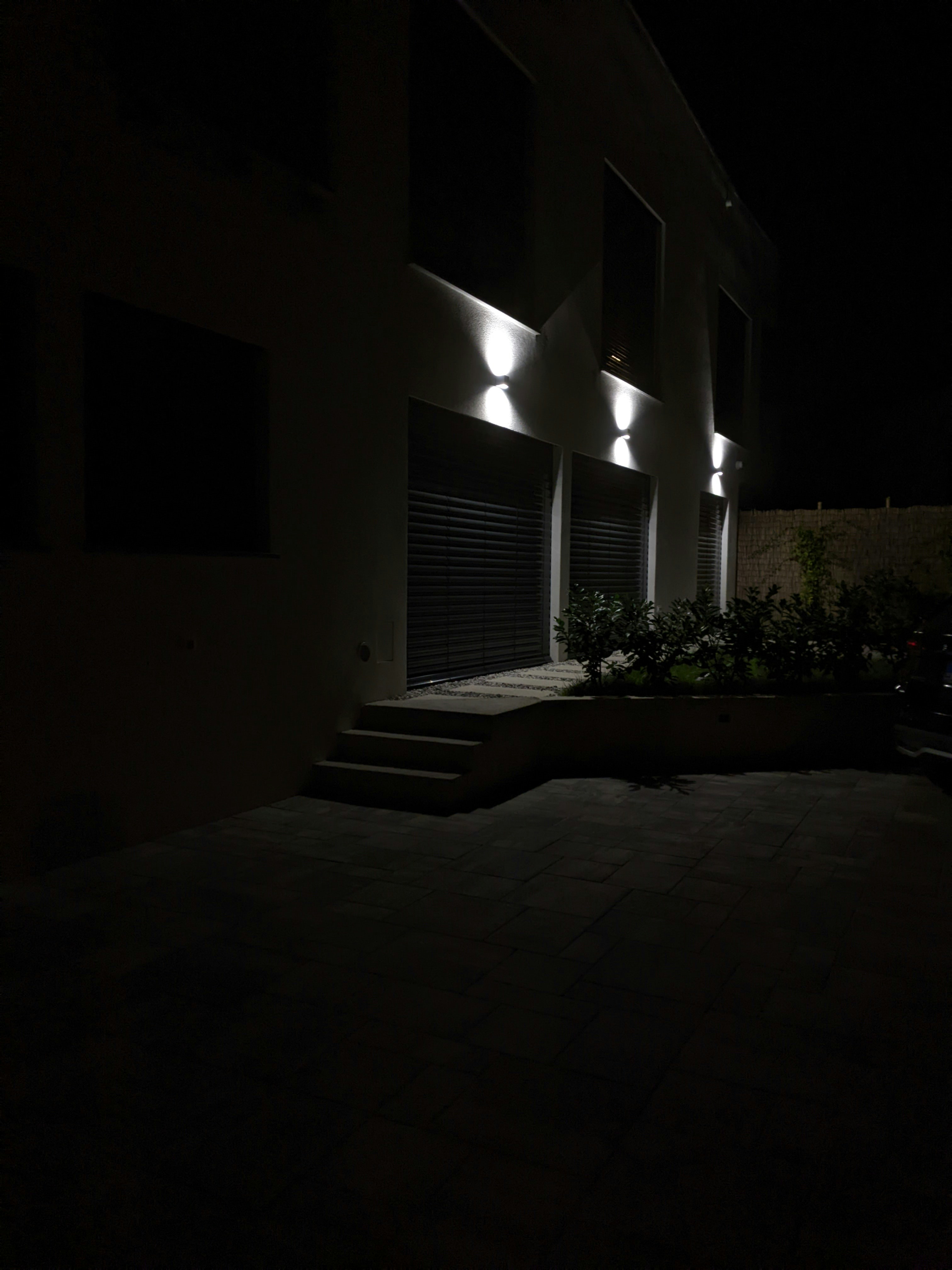 Modern luxury home exterior at night, deep shadows on facade, dramatic architectural lighting, dark sky