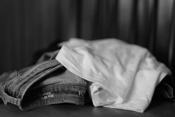 A neatly folded stack of minimalist men's shirts and pants on a wooden table.
