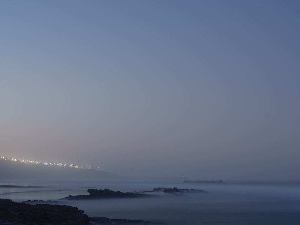 a foggy night at the beach with a light house in the distance