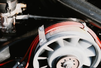 A detailed view of a mechanical component featuring a fan-like structure with visible metallic bolts and nuts. It is surrounded by a loop of red electrical wiring labeled as spark plug wire, set against a background of additional mechanical parts.