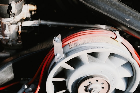 A detailed view of a mechanical component featuring a fan-like structure with visible metallic bolts and nuts. It is surrounded by a loop of red electrical wiring labeled as spark plug wire, set against a background of additional mechanical parts.