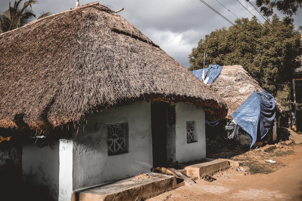 a thatched roof house with a blue tarp on the roof