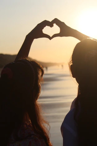 two women making a heart shape with their hands