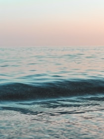 A calm shoreline at dawn with gentle waves reflecting soft pastel colors.