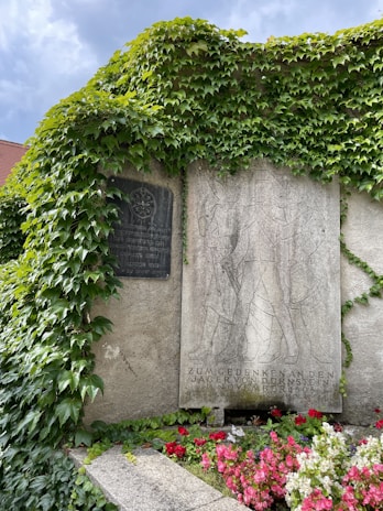 A gentle hand placing a QR code plaque on a weathered gravestone surrounded by blooming flowers.