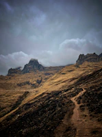 Wide shot of rugged mountain terrain with runners ascending steep rocky paths.