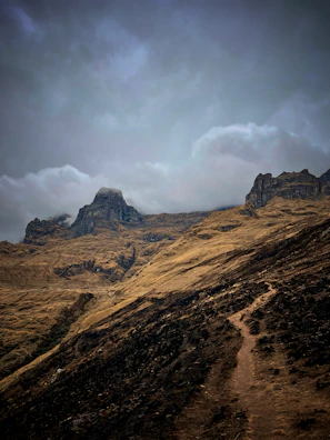 Wide shot of rugged mountain terrain with runners ascending steep rocky paths.