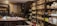 A cozy tea shop interior with shelves lined with neatly stacked tea packages. A large wooden table is set with teaware, teacups, and a bowl of grapes. Various pottery and decorative items are displayed around the room, giving a traditional and inviting atmosphere.