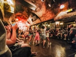 An underground jazz club with an arched ceiling and lively atmosphere. People are dancing in the center, while others sit around enjoying the music from a live band on the stage.