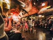 An underground jazz club with an arched ceiling and lively atmosphere. People are dancing in the center, while others sit around enjoying the music from a live band on the stage.
