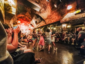 An underground jazz club with an arched ceiling and lively atmosphere. People are dancing in the center, while others sit around enjoying the music from a live band on the stage.