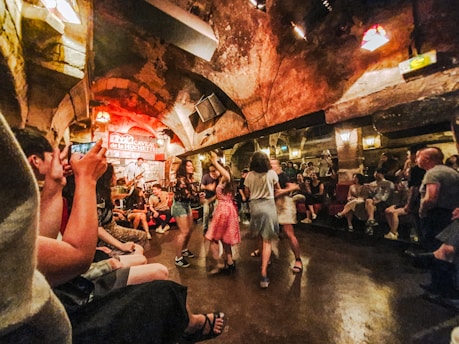 An underground jazz club with an arched ceiling and lively atmosphere. People are dancing in the center, while others sit around enjoying the music from a live band on the stage.