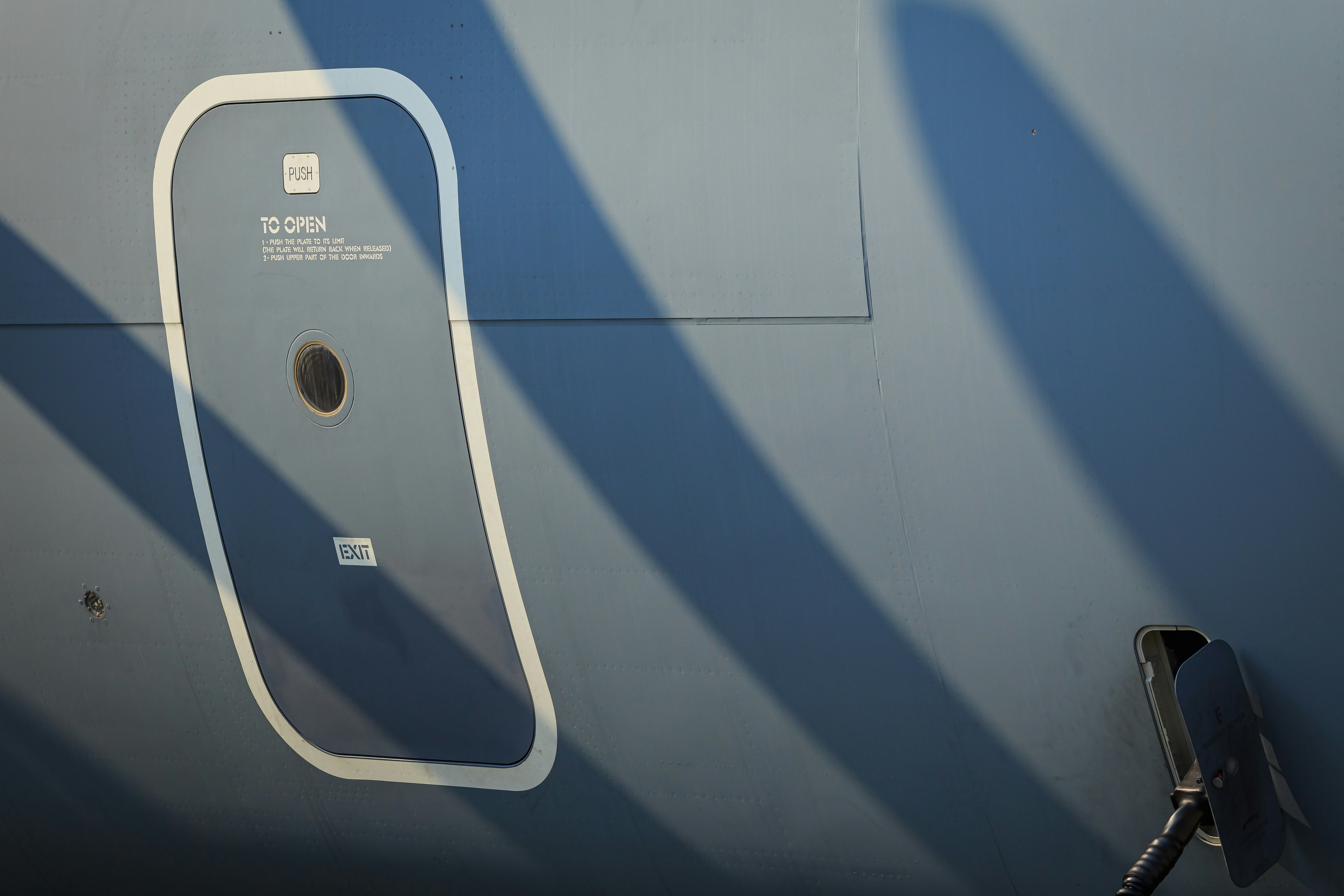 a close up of a gas pump on the side of a plane, Military transport aircraft door with propeller shadows