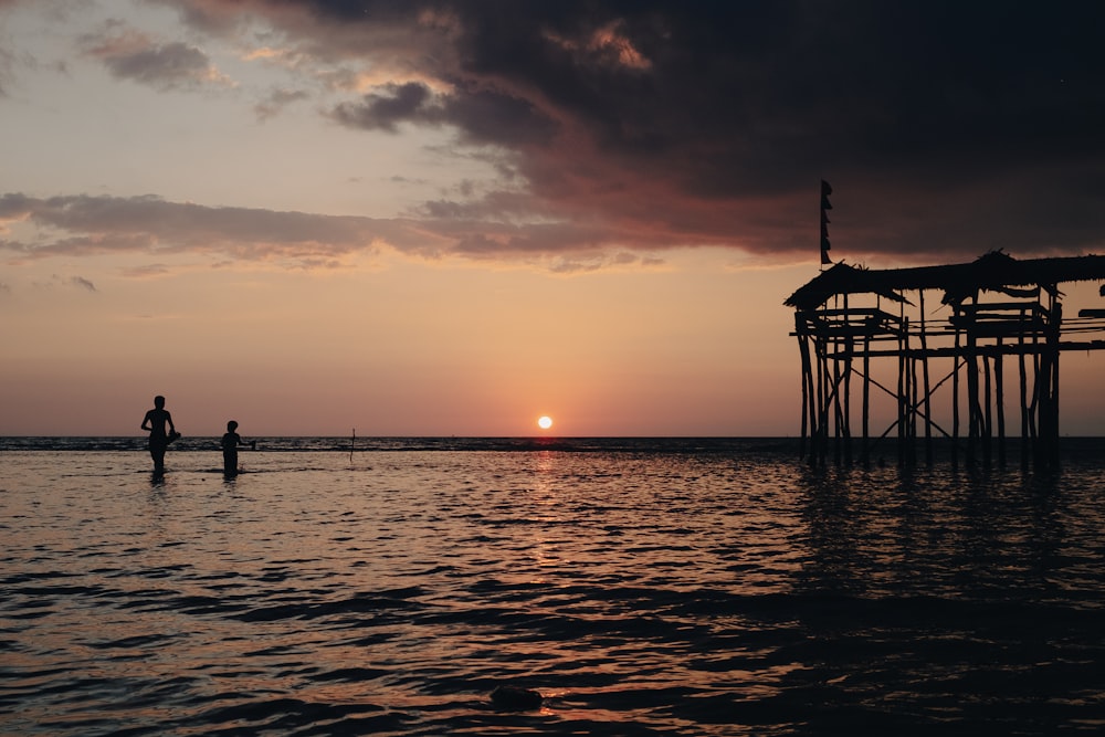 a couple of people in a body of water at sunset