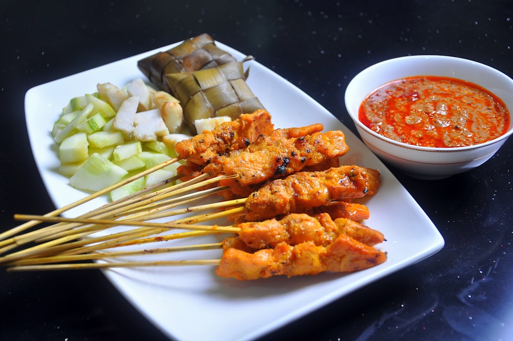 a white plate topped with meat and veggies next to a bowl of sauce