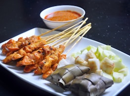 a white plate topped with meat and veggies next to a bowl of sauce