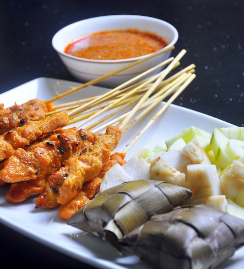 a white plate topped with meat and veggies next to a bowl of sauce