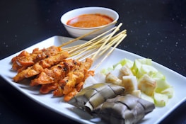 a white plate topped with meat and veggies next to a bowl of sauce