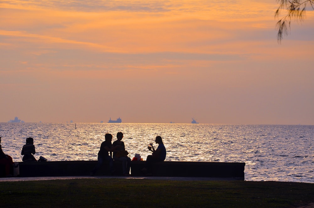 a group of people sitting on a bench next to the ocean
