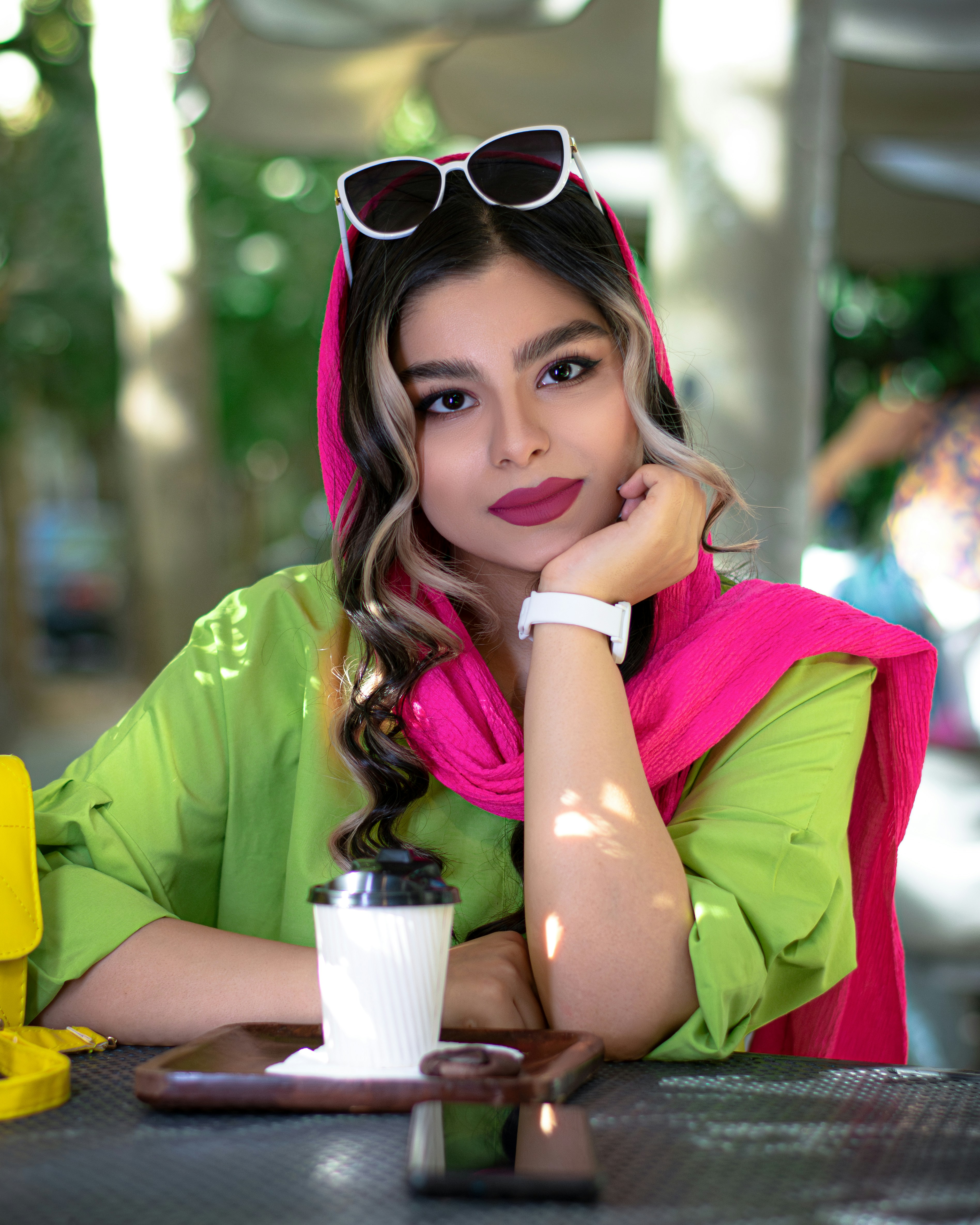 seorang wanita dengan syal merah muda dan kacamata hitam duduk di meja