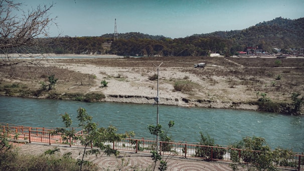 An engineer reviewing blueprints beside a flowing river surrounded by green trees.