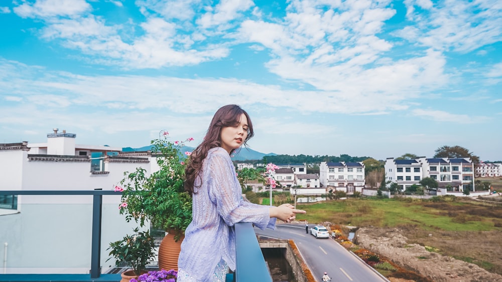 a woman standing on top of a balcony next to a plant