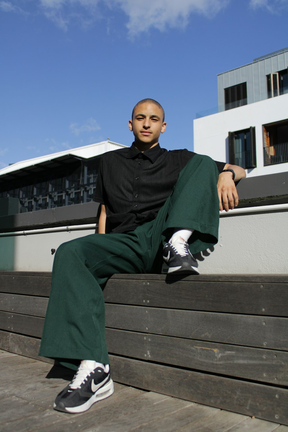 a man sitting on a wooden bench wearing a black shirt and green pants