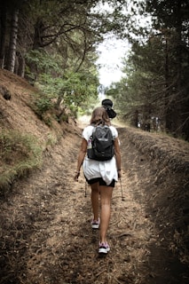 a woman with a backpack walking down a dirt road