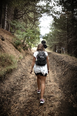 a woman with a backpack walking down a dirt road