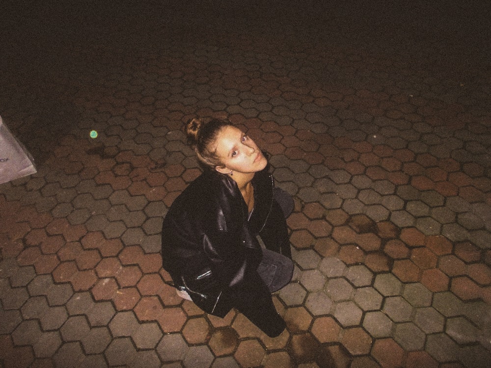 a woman sitting on the ground in a black jacket