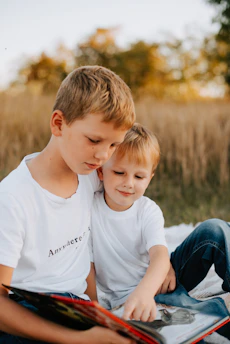 two young boys sitting on a blanket reading a book