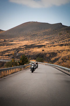 A group of motorcyclists riding through winding mountain roads at sunset.