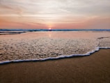 A serene beach at sunset with gentle waves lapping the shore.